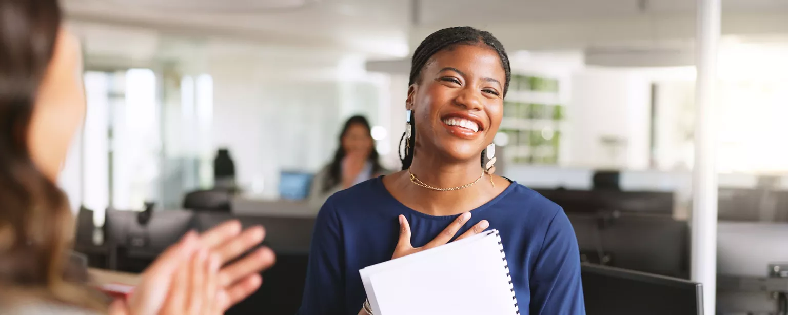 Administrative professional smiling and receiving recognition from a colleague.