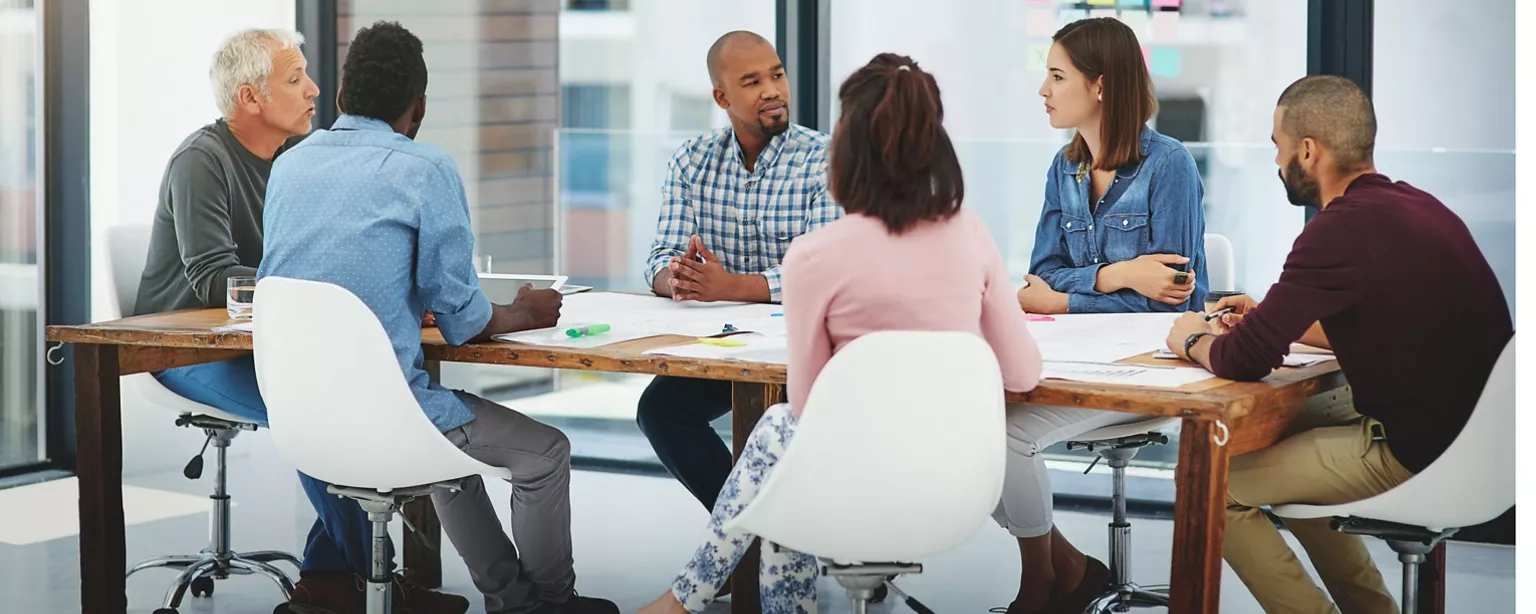 A project team sits around a table in a conference room, discussing project status.