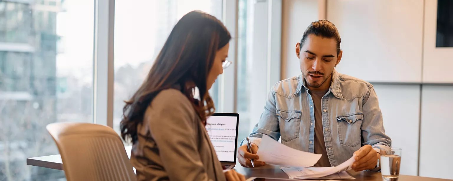 Two hiring managers sitting in an office are reviewing the resumes of potential job candidates.