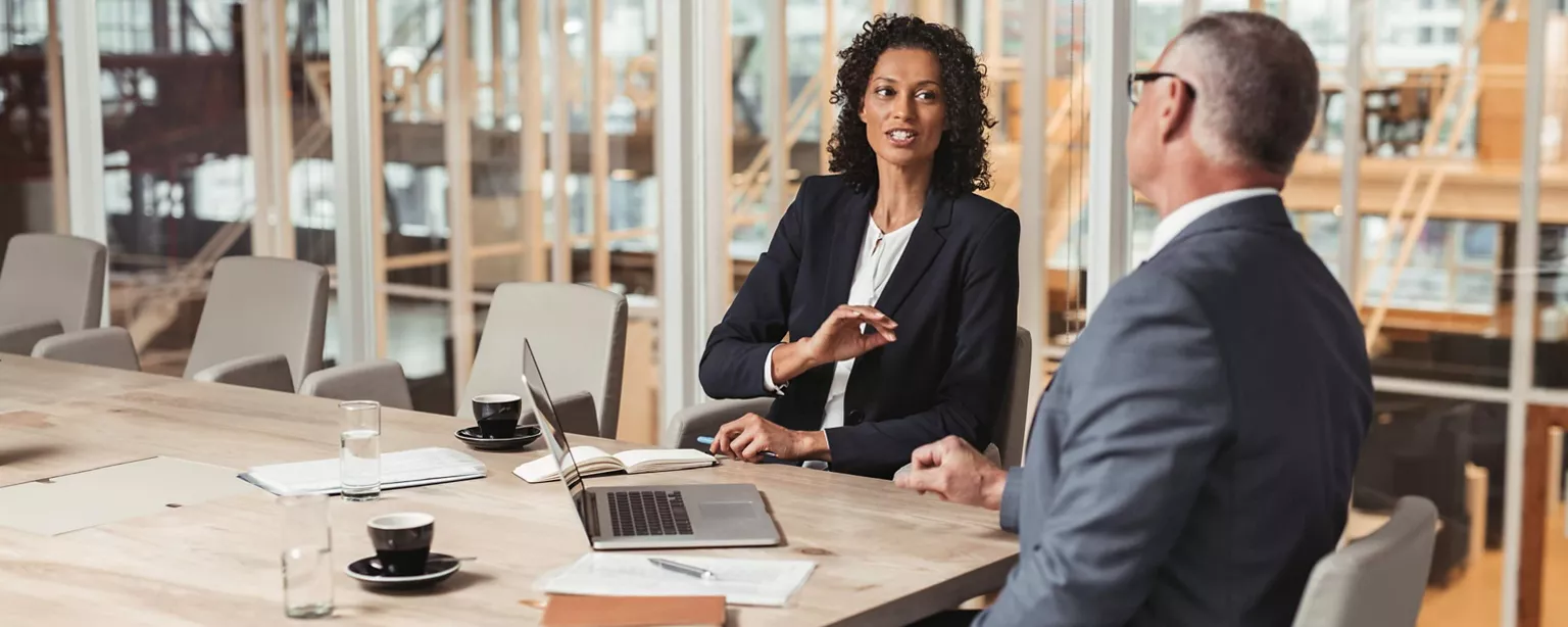 Two senior executives, a woman and man, sit in a conference room to discuss succession planning strategy for the business.