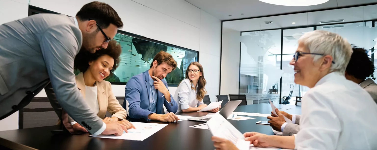 A multigenerational team of employees in a small business collaborates on a project while meeting in a conference room.