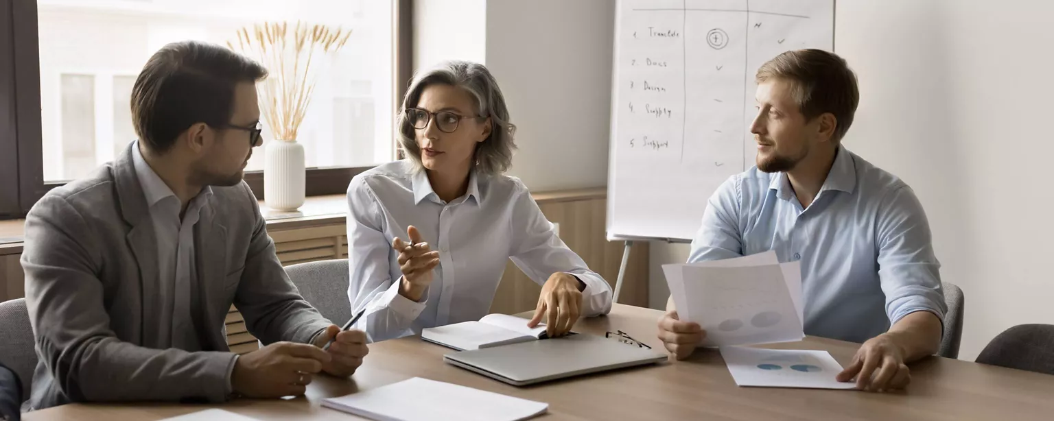 A small business consultant leads a meeting with two financial staff members at a small business.