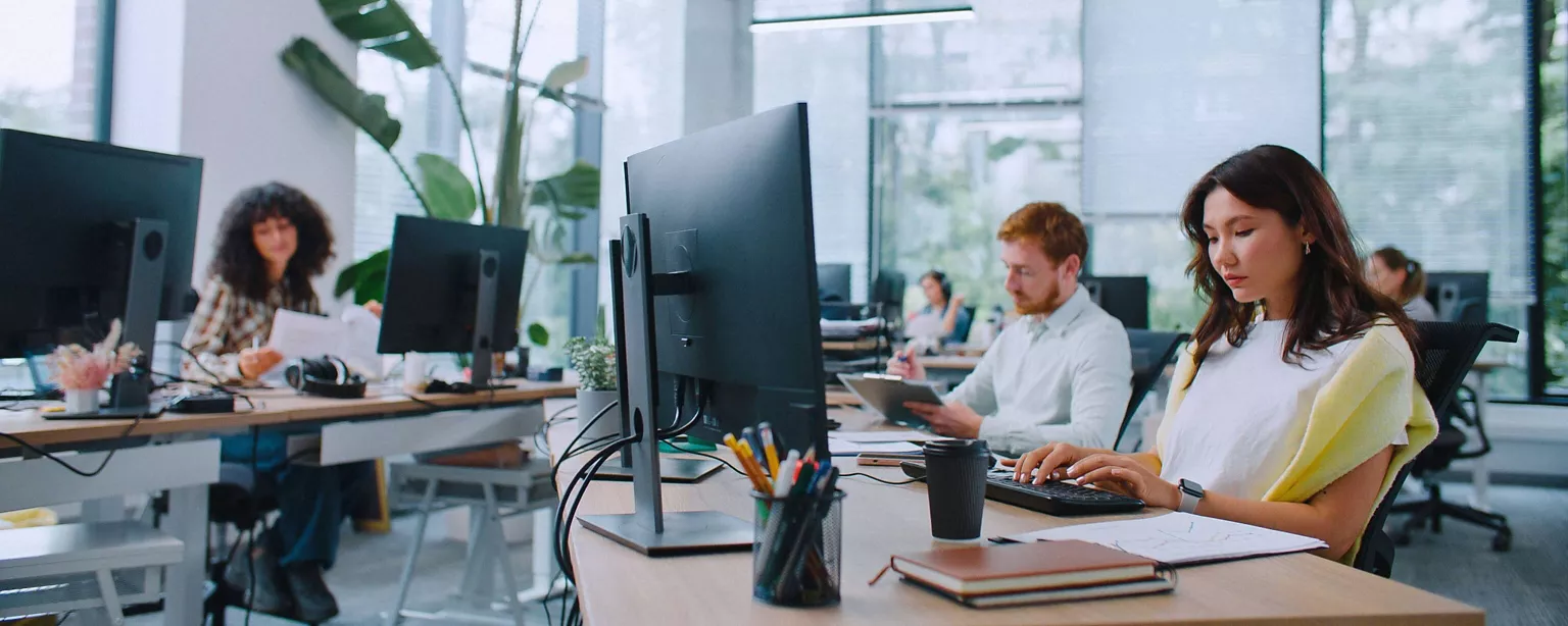 Employees at work in a modern office, sitting at workstations and typing on computer keyboards or looking at papwerwork.