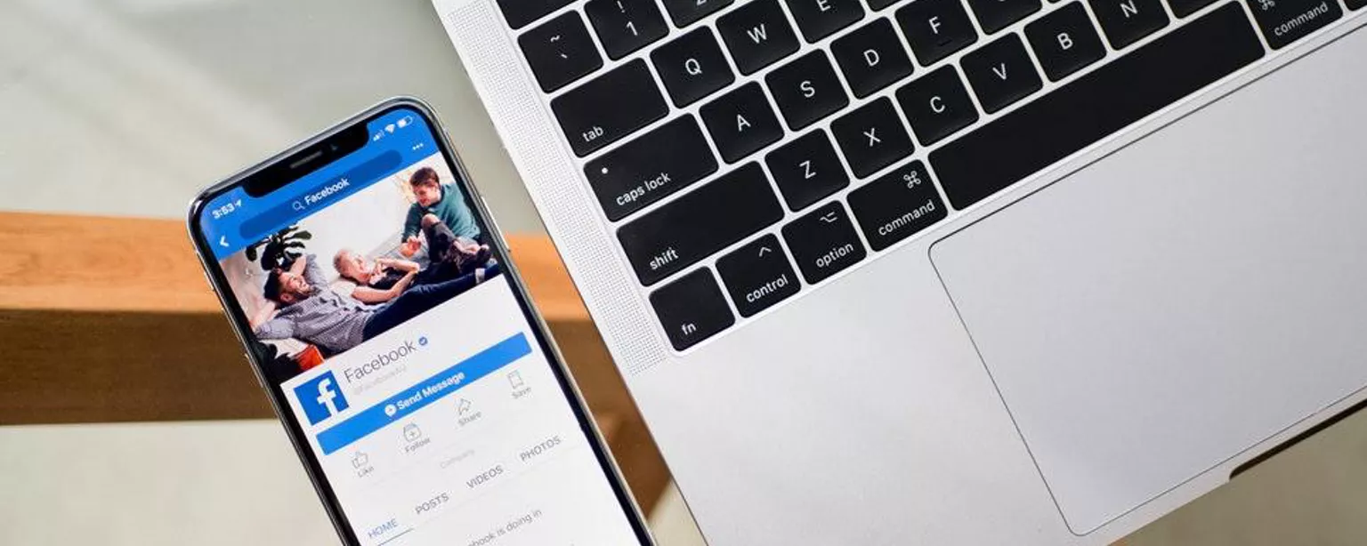 celular com facebook aberto em tela, ao lado de um notebook