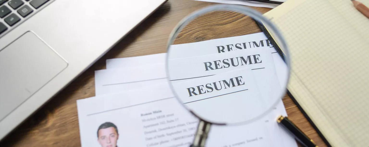 Resumania®: Sum It Up and Skip the Objective Statement — magnifying glass over the word RESUME on paper