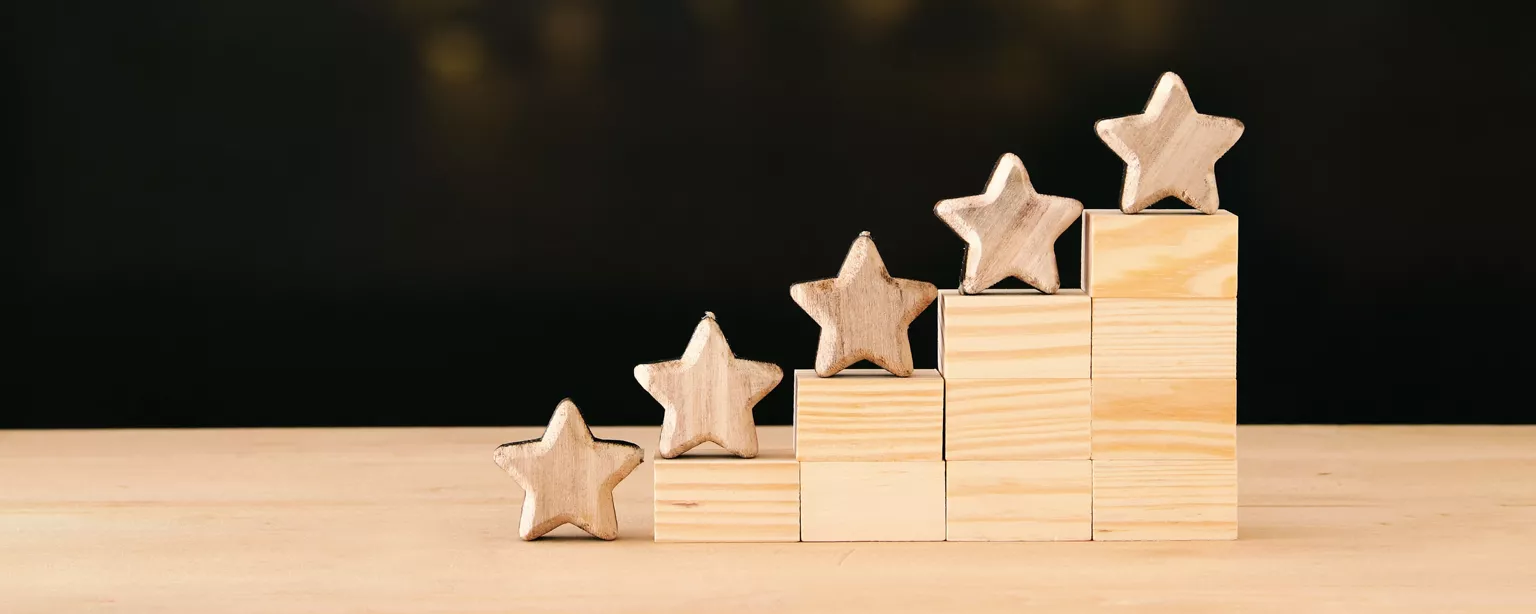 Tiered wooden blocks with wooden stars on top and lights in the background.