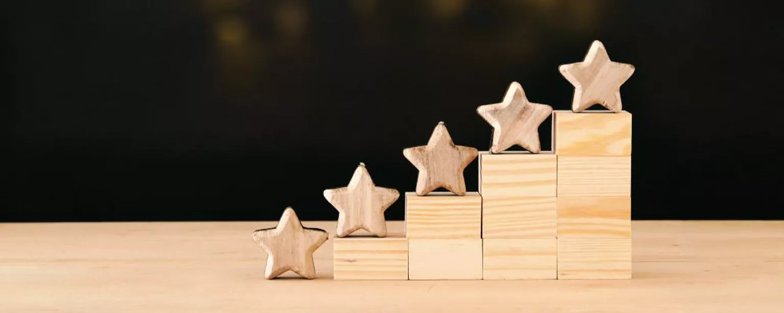 Wooden stars on stepped blocks from lowest to highest. Blurred lights are in the background