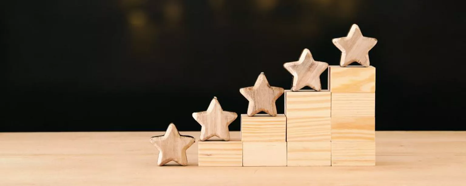 Tiered wooden blocks with wooden stars on top and lights in the background.