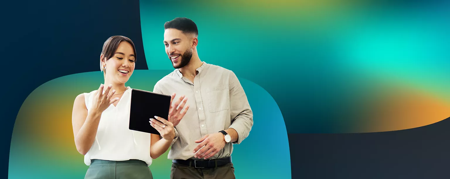 A woman and a man stand next to each other looking at a tablet and smiling.
