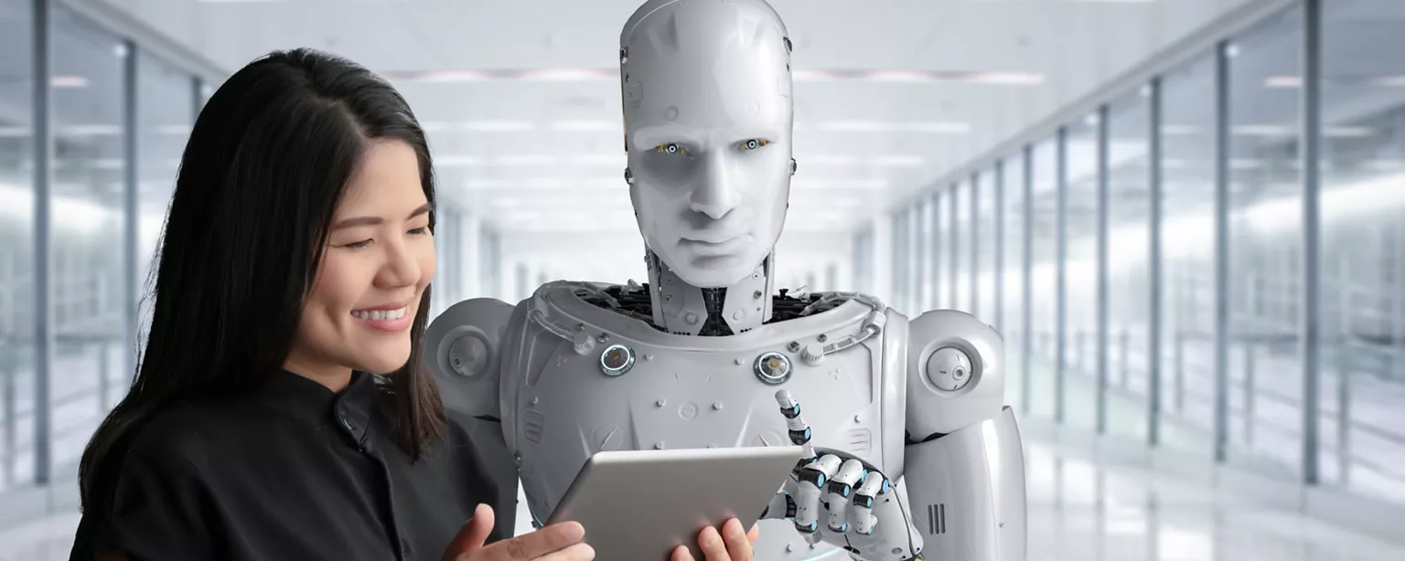 Happy woman and humanoid robot stand looking at laptop screen together