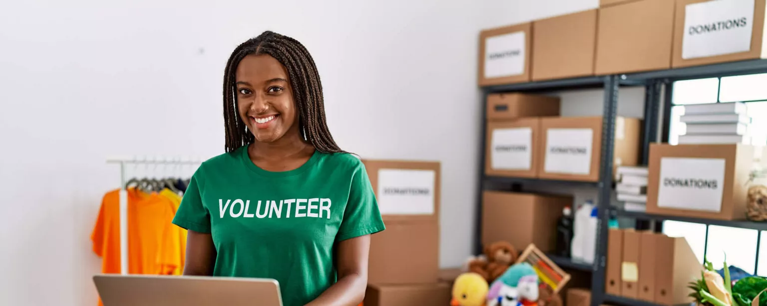 Woman wearing green shirt with words VOLUNTEER stands next to DONATIONS box