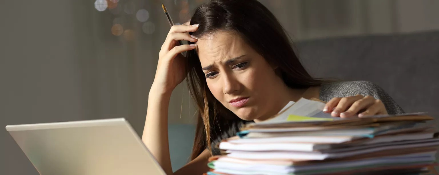 A hiring manager appears overwhelmed as she sorts through resumes in front of her computer.