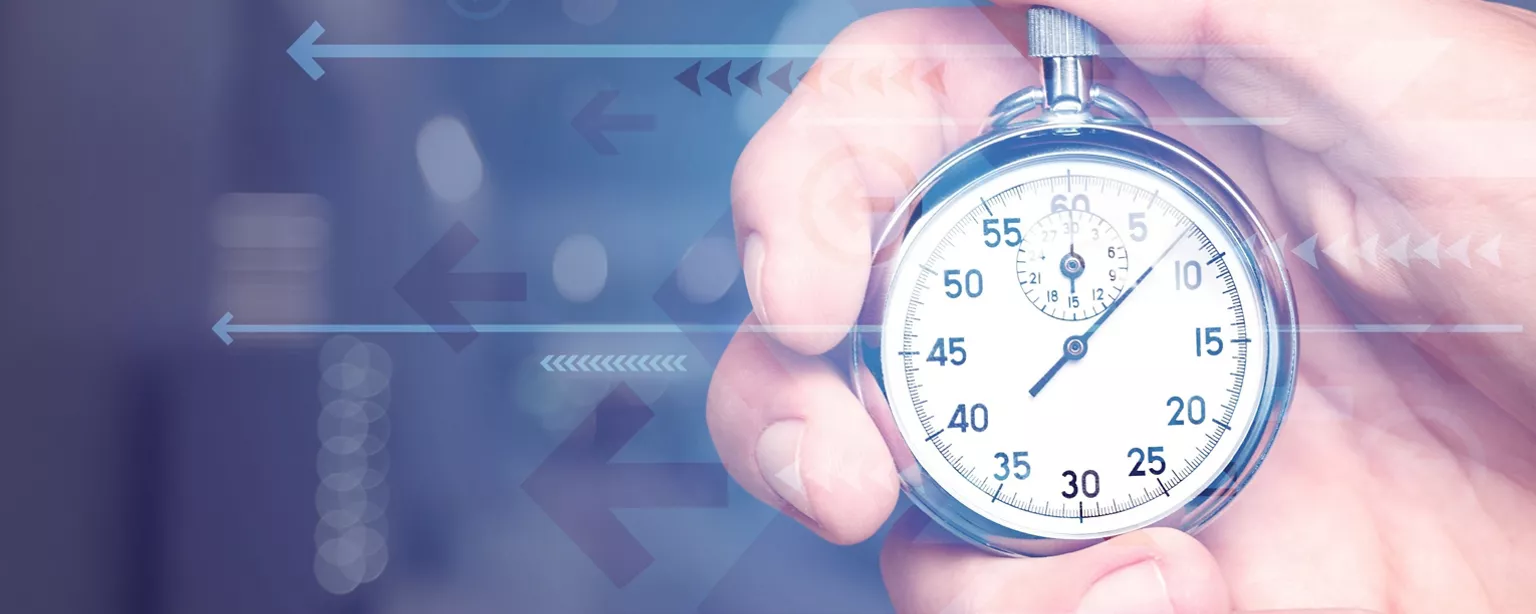 A person's hand holds a silver stopwatch against a dark background with shadows of arrows.