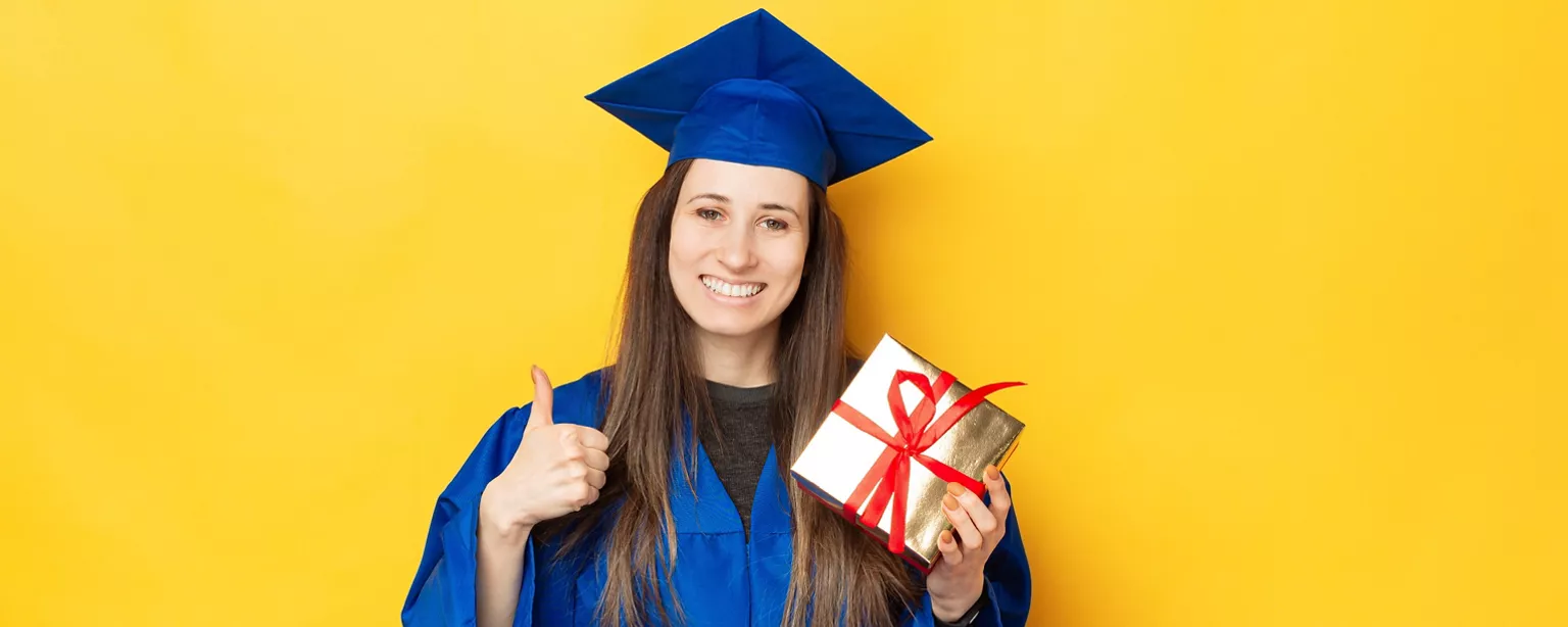 A recent college graduate wearing a blue cap and gown holds a gift-wrapped box containing a book.
