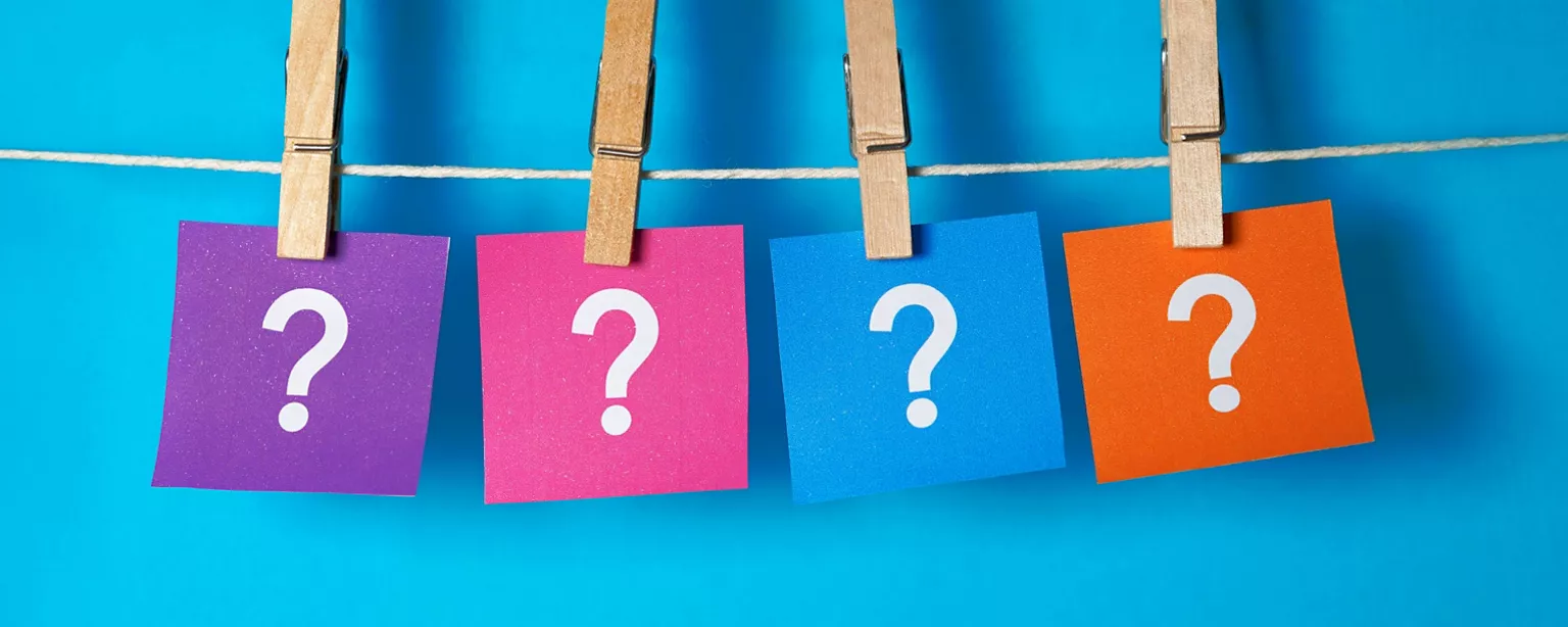  Four sticky notes in different colors purple, pink, blue and orange with a white question mark on each clothespinned to a string on a medium blue background.