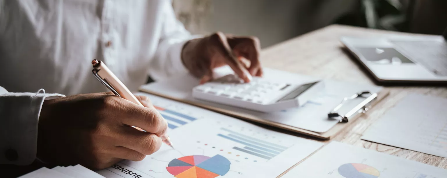 A person reviewing financial charts and using a calculator at a desk, analyzing year-end accounting data.