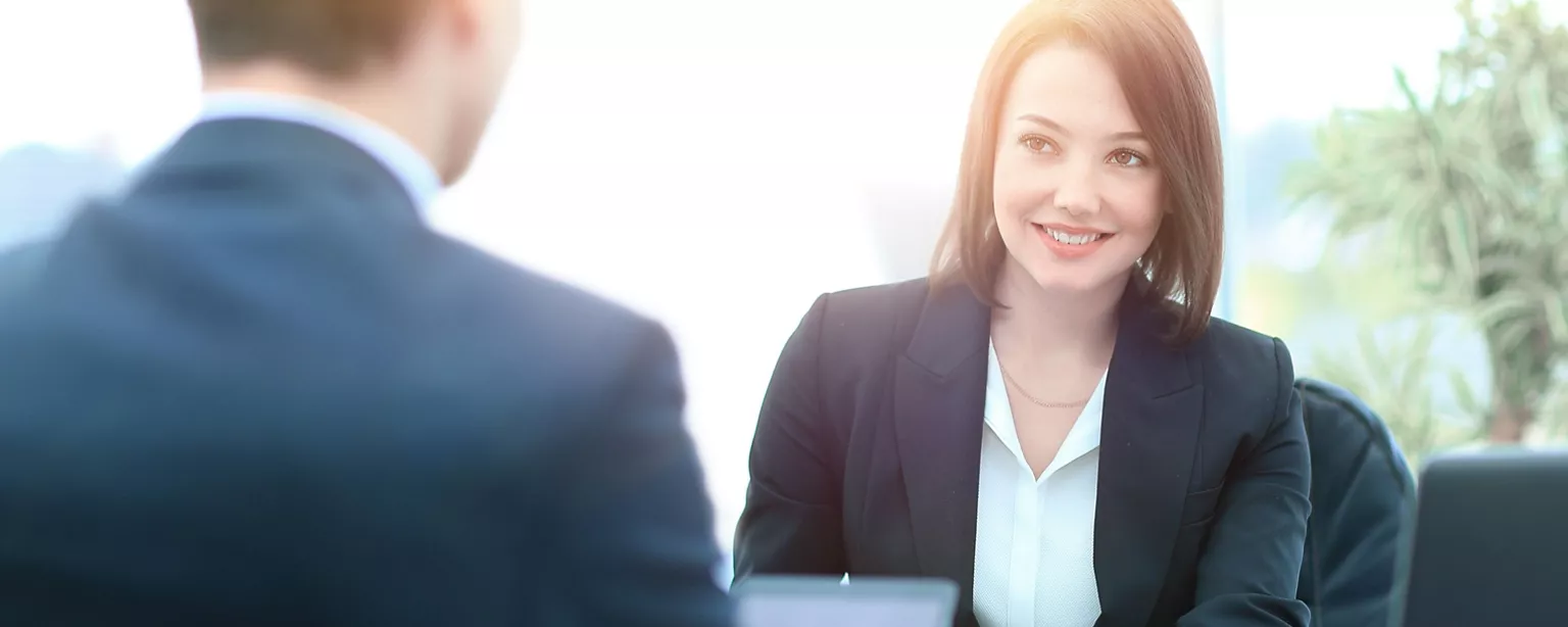 A smiling job candidate sits at a desk across from the interviewer.