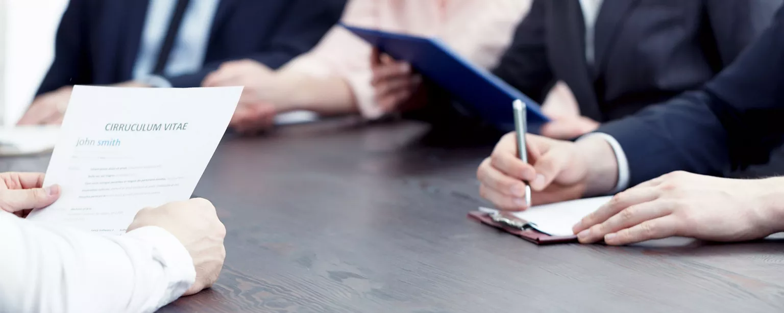 Person sitting at desk holding resume across from three people in suits.