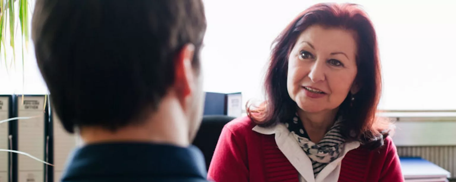 A candidate applying for a business analyst job sits across the desk from the woman who is interviewing him.