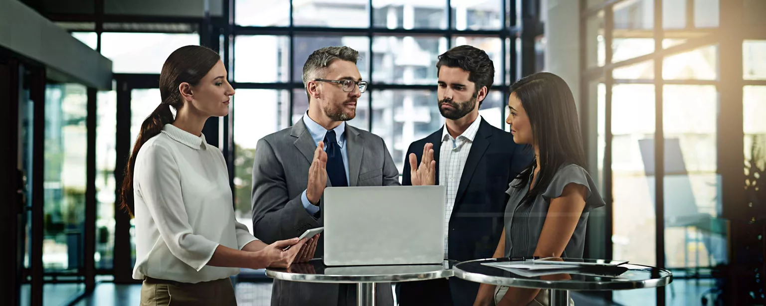 A small business leader is having a discussion about strategy with his employees while standing in front of laptop.