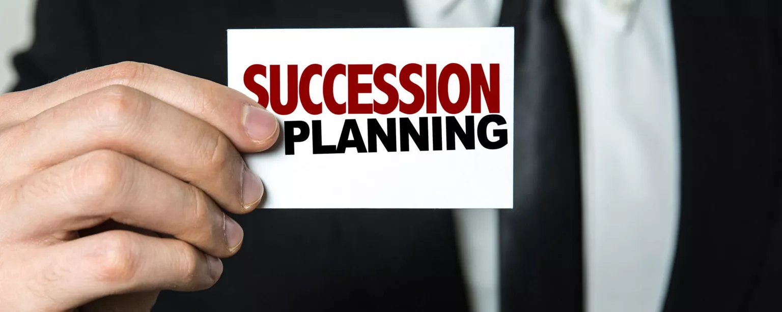 A man in a black suit holds a card that reads "SUCCESSION PLANNING."