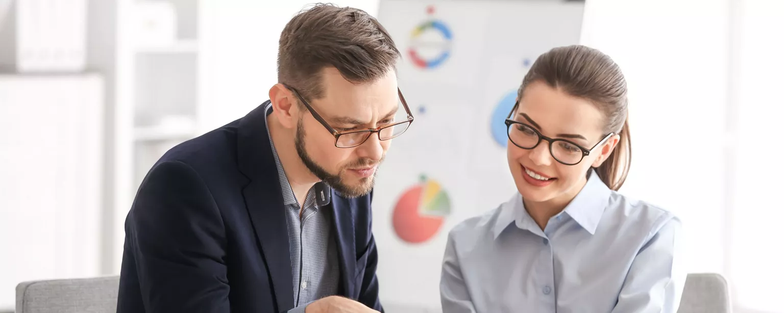 A man and woman sitting at an office table and looking at a report.