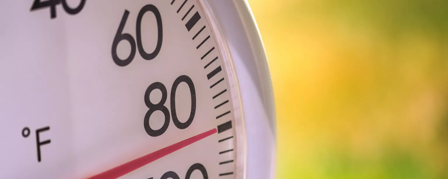 White and black temperature gauge displays a red needle at 90 degrees Fahrenheit as it approaches 100; gauge is set against a yellow and green background.