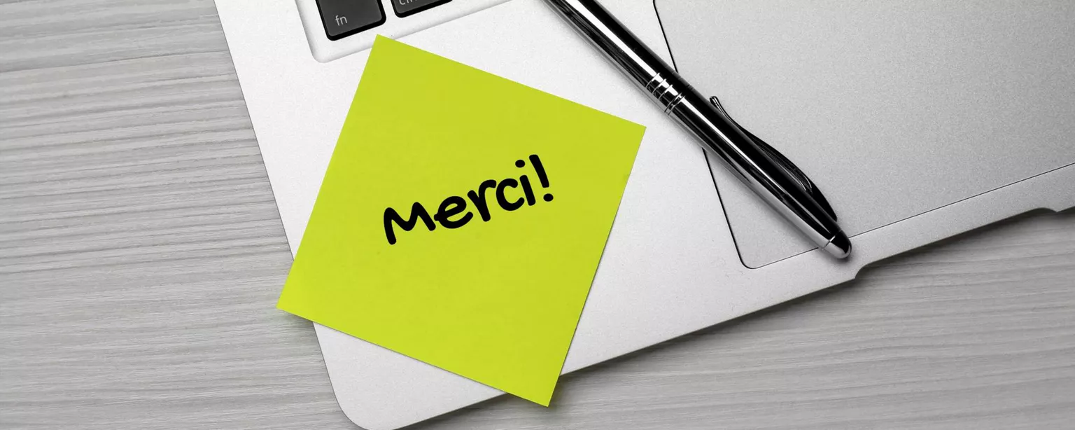 Vue de dessus du mot "merci" écrit sur une note autocollante placée à côté d'un stylo sur le clavier d'un ordinateur portable.