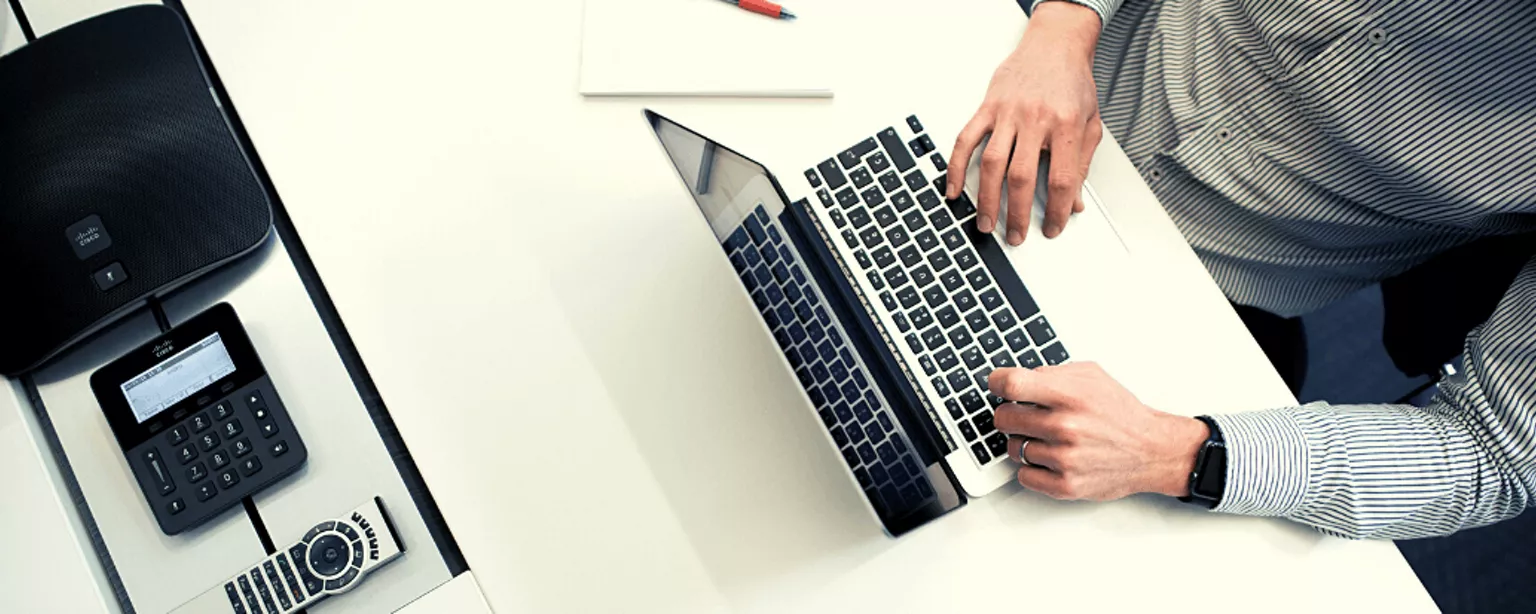 Person tippt auf Laptop, daneben liegen Stifte und ein Taschenrechner.