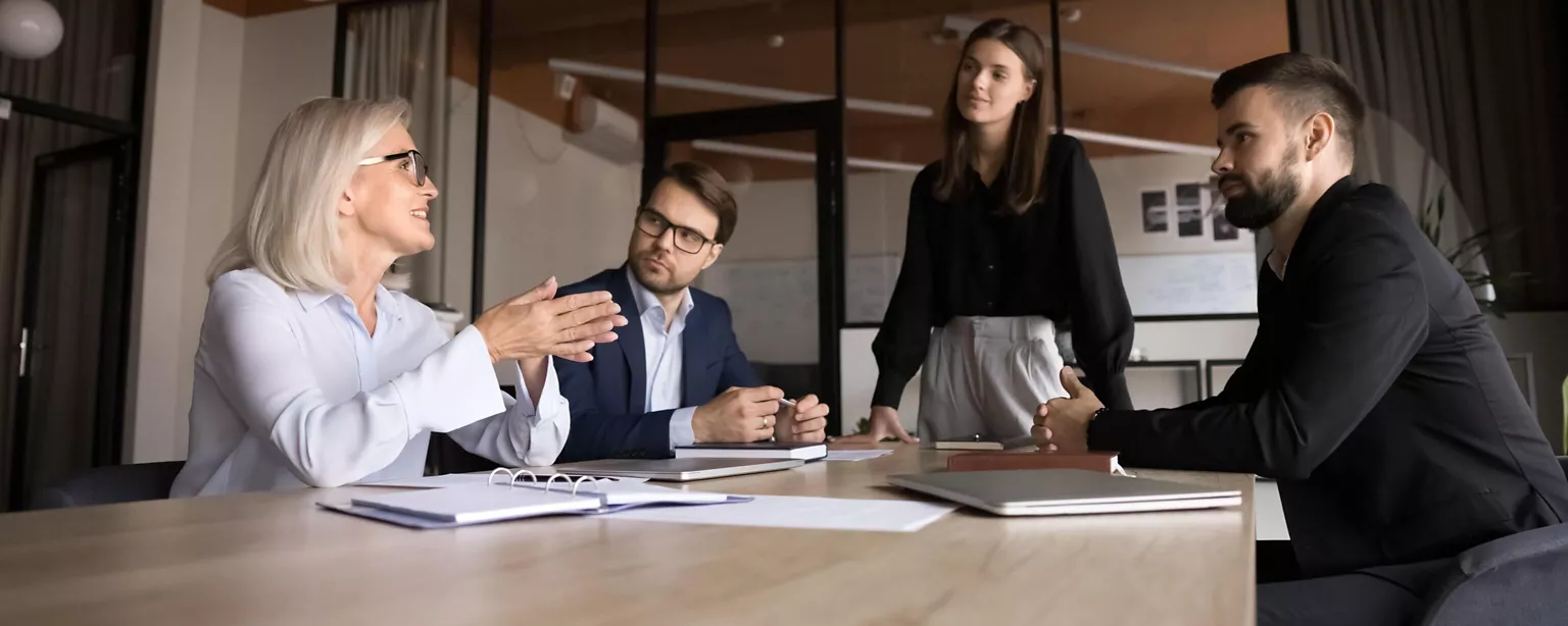 A small business leader has a heart-to-heart conversatin with her employees in a conference room, asking them about their work preferences.