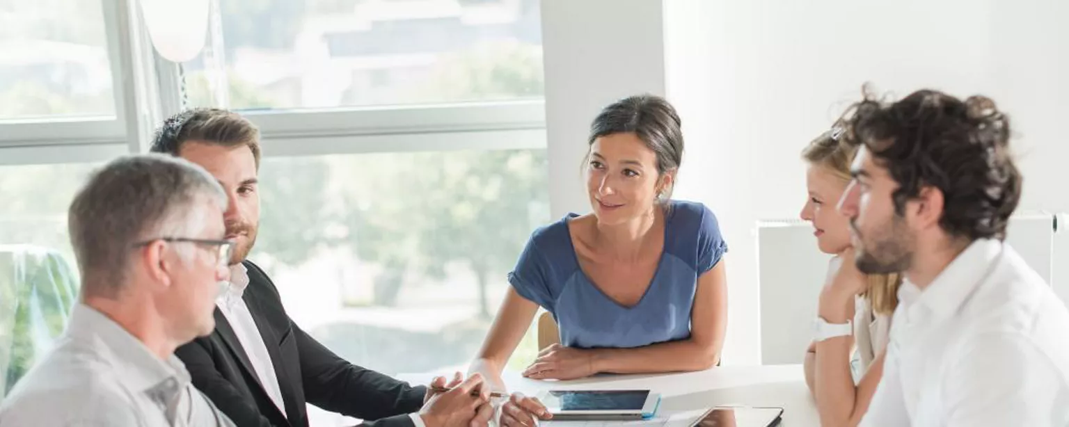 Équipe d'affaires assise à une table blanche dans une salle de conférence en réunion avec un consultant.