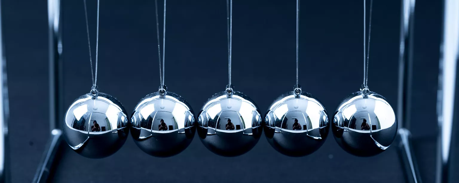 Five silver balls in a Newton's cradle hang in perfect alignment.