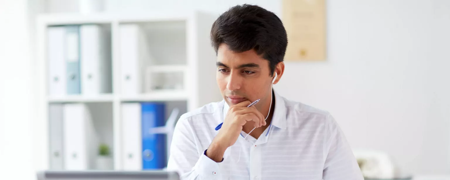 A young man in a white shirt looking at a laptop and engaging in online learning.