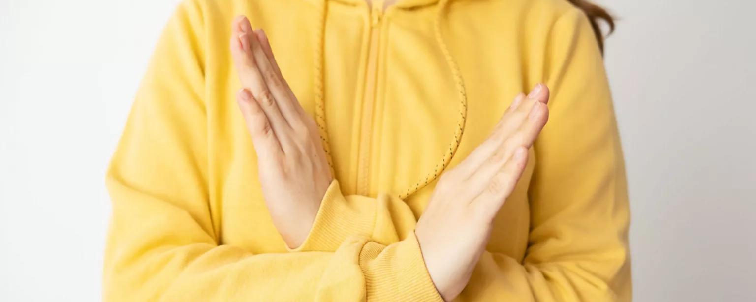 A woman in a yellow sweatshirt, crossing her wrists to symbolize #BreakTheBias, the 2022 theme for International Women's Day.