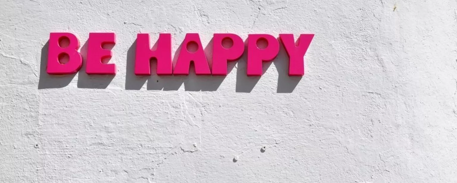 Pinker Schriftzug "Be Happy" auf weißer Wand