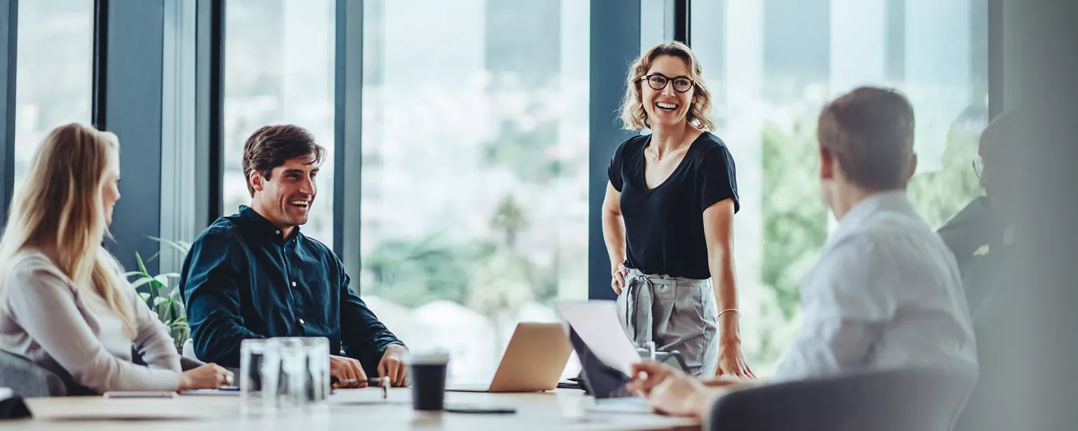 Team members smile around a conference table with natural light coming through the windows.