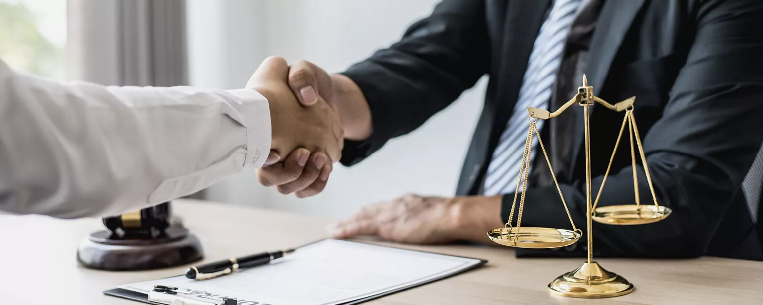 Two people shaking hands while sitting at a desk.
