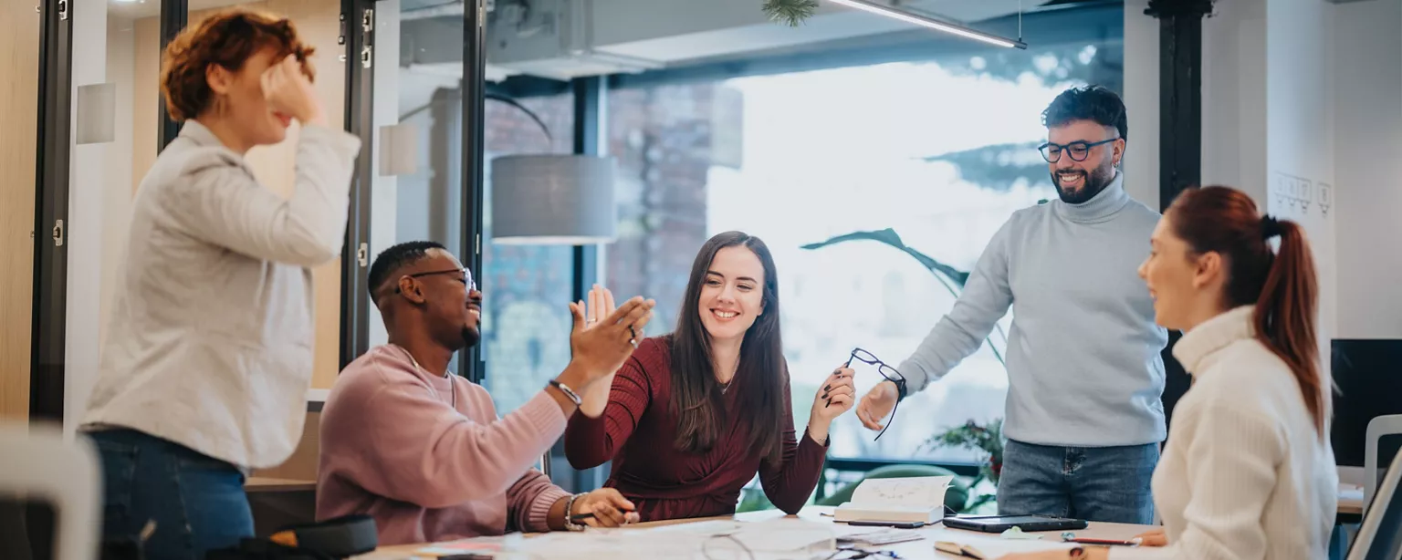 Team members celebrate a successful collaboration with smiles and high-fives in a bright office.