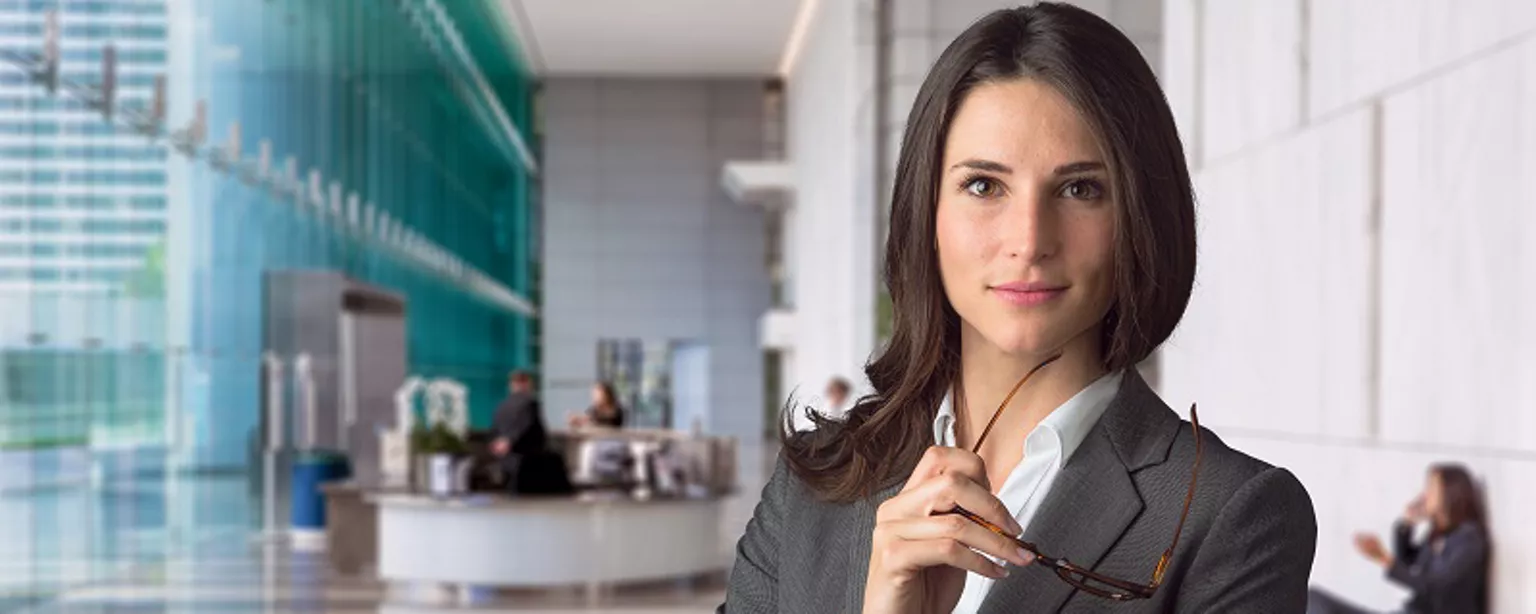 business woman standing at reception area of large office building holding her glasses