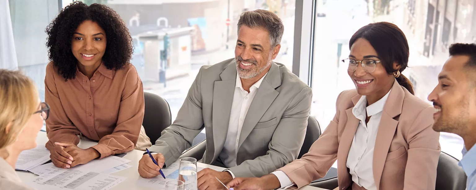 A group of business leaders sits around a conference table, smiling and reviewing documents during an advisory board meeting.