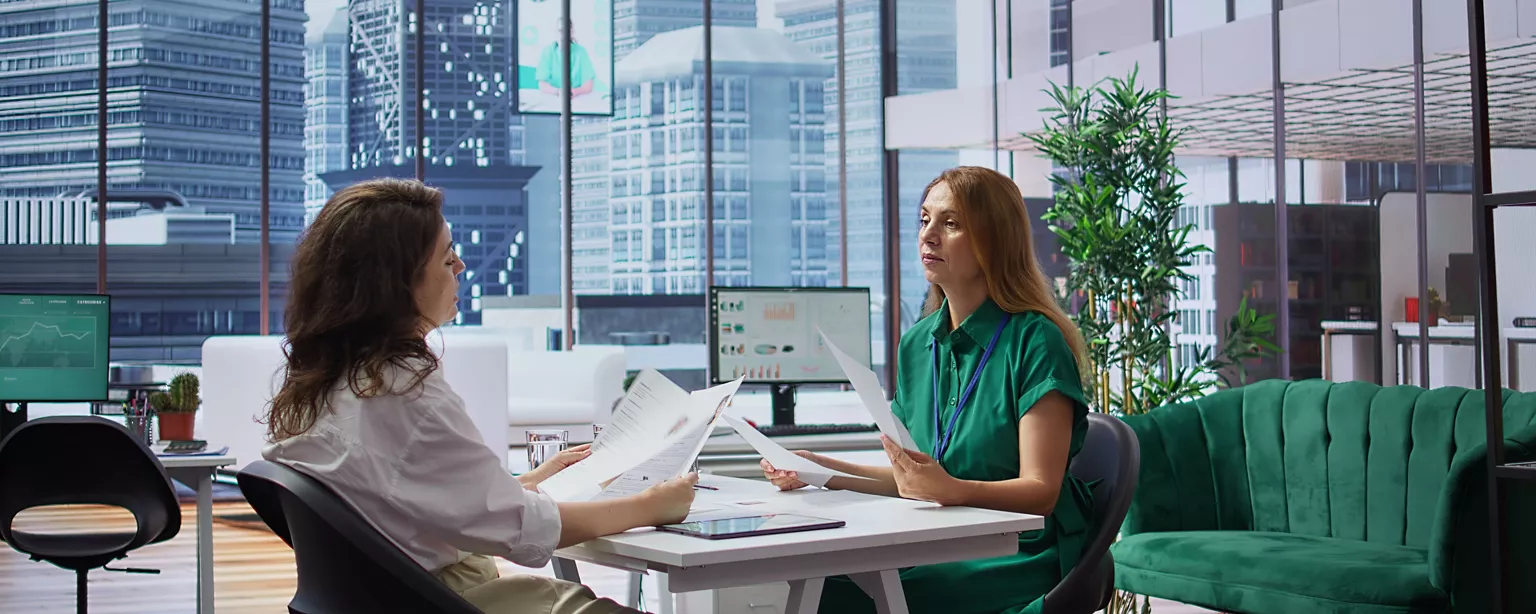 Hiring managers for a finance firm review candidate resumes in a high-rise office.