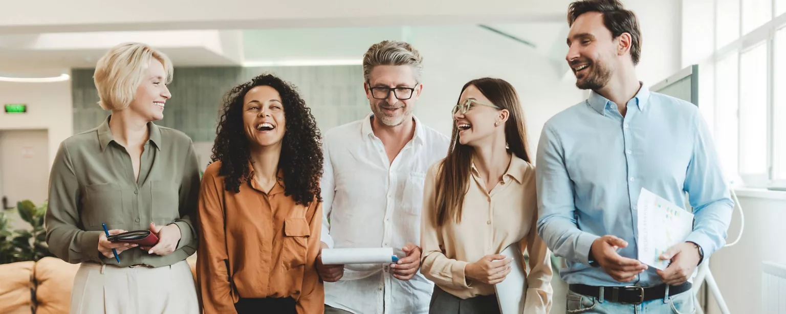 Five members of the multigenerational workforce stand side by side in an office environment.