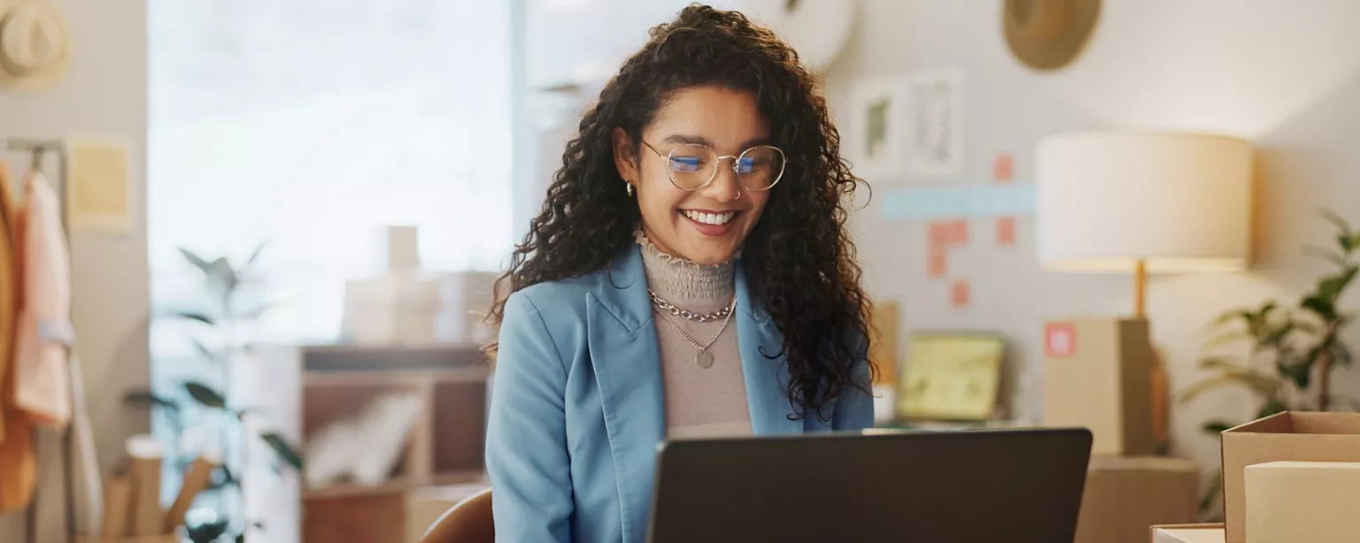 A professional woman smiling while working on a laptop in an office.