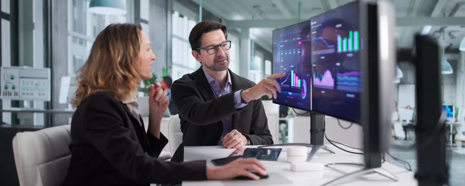 Colleagues in a finance and accounting department discuss the results of AI analysis of financial data displayed on a computer screen.