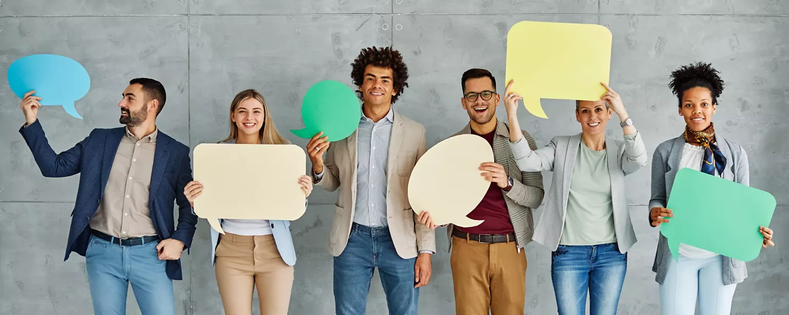 A group of professionals smiling and holding colorful speech bubble cutouts.