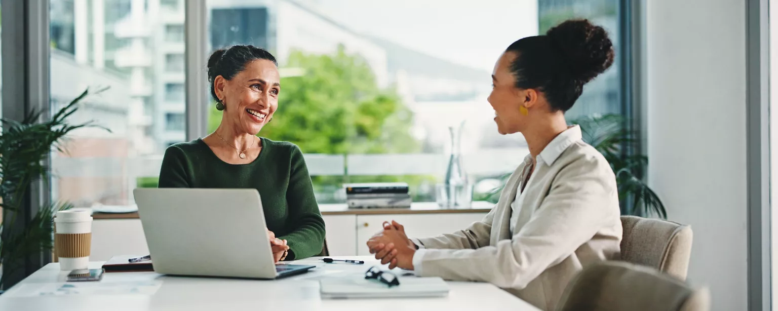 A manager and employee having a one-on-one meeting at a desk with a laptop, discussing performance and feedback.