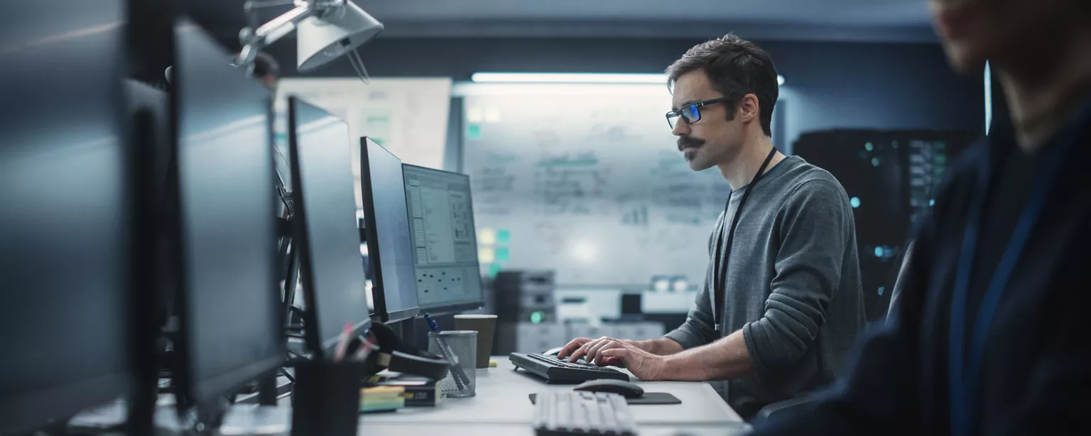 A cybersecurity professional works intently at a multi-monitor setup in a high-tech operations center.