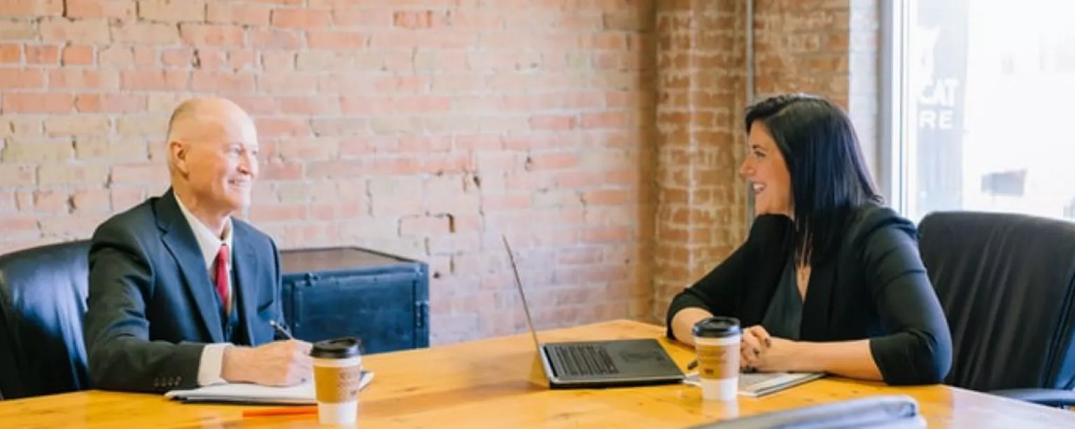 A man and woman in business attire sit at a meeting table