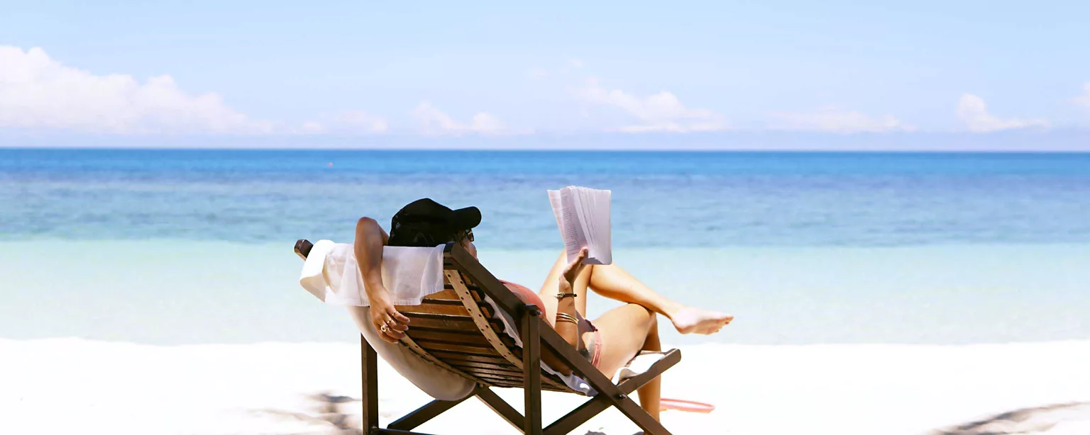 Frau liegt im Liegestuhl am Strand und liest ein Buch
