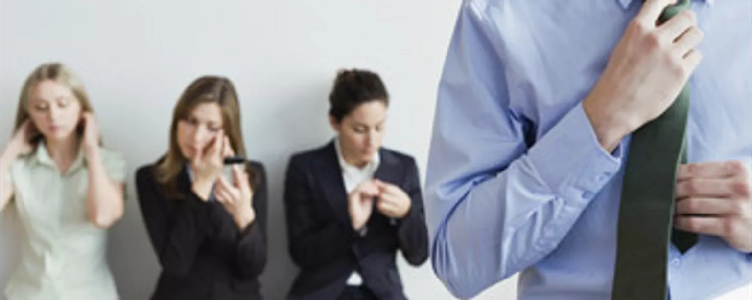 Man adjusting tie as he waits with three others for a job interview